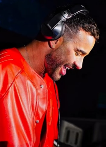 Un hombre con barba de perfil lleva auriculares negros y ropa roja sobre un fondo oscuro