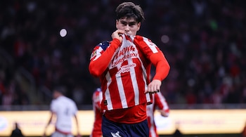 Joven futbolista en camiseta de rayas rojas y blancas con patrocinadores, mangas rojas y shorts azules, levanta la tela hacia su boca en estadio.