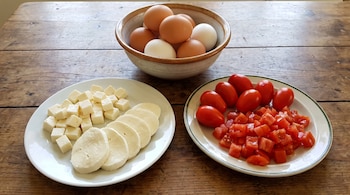 Una compotera con huevos, un plato con mozzarella en cubos y rodajas, y un plato con tomates enteros y picados sobre una mesa de madera.