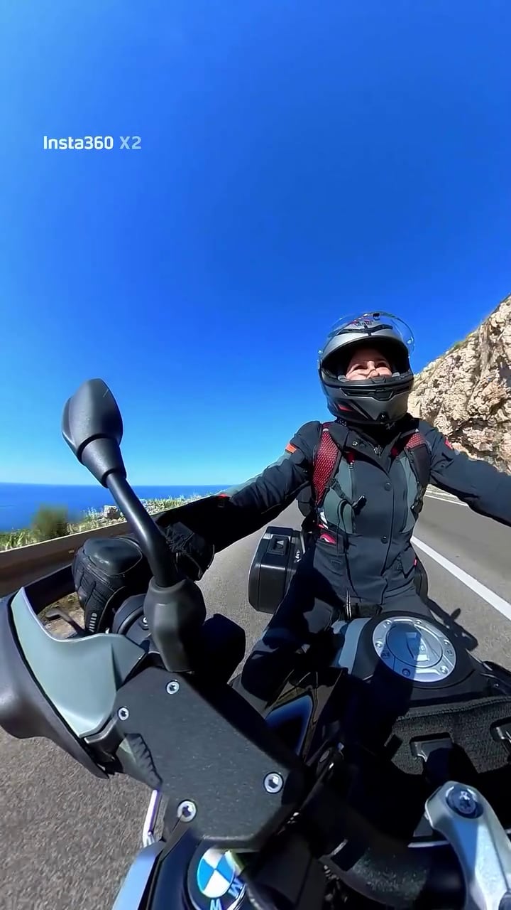 Carolina Baldini disfruta la libertad de su travesía en moto desde Croacia a Grecia, viajando por una carretera costera bajo un cielo azul brillante.