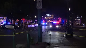 Vista nocturna de una calle acordonada con cinta amarilla, mostrando tres vehículos policiales con luces intermitentes y escombros en el pavimento
