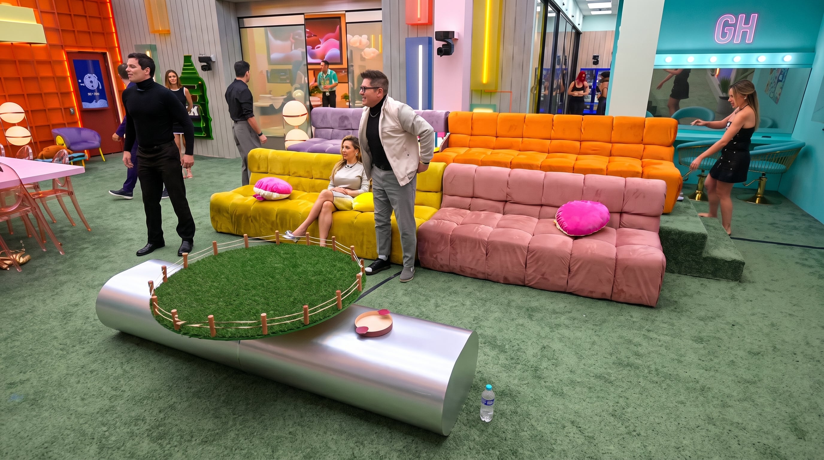 Participantes de un programa de televisión se encuentran en un set colorido con sofás modulares, alfombra verde y una mesa central con diseño de césped. (Imagen Ilustrativa Infobae)