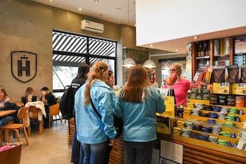 En el interior de un café, personas con chaquetas celestes de ARBA y una con camiseta del Ministerio de Trabajo conversan con una empleada detrás del mostrador lleno de productos