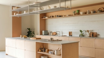 Vista general de una cocina moderna y espaciosa con una isla central de madera clara, encimeras grises y estantes flotantes con objetos de cerámica.