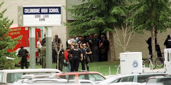 Vista exterior de la Escuela Secundaria Columbine, con un cartel, ambulancia y numerosos oficiales de policía y personal de emergencia frente al edificio