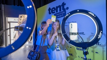 Dos mujeres posan frente a teléfonos celulares montados en aros de luz iluminados ante un panel con la inscripción Tent Creator Summit