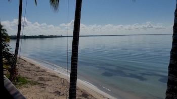 Vista panorámica de una playa de arena clara y aguas tranquilas bajo un cielo azul con nubes blancas, enmarcada por palmeras. No hay personas