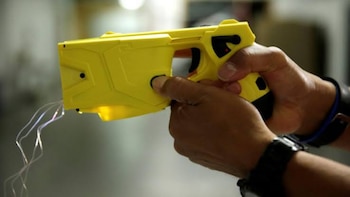 Una persona sostiene con ambas manos una pistola de electrochoque de color amarillo de la cual salen cables delgados