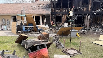 Vista exterior de una casa residencial con la mitad de su estructura carbonizada por un incendio y la otra mitad parcialmente intacta, con escombros en el césped