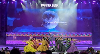 Bailarines vistiendo atuendos tradicionales realizan una coreografía frente a una gran pantalla azul con la inscripción Primera Luna