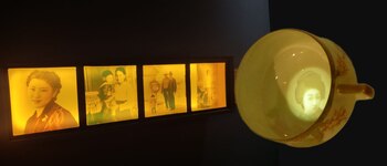 Cuatro fotografías antiguas iluminadas en un marco de madera junto a una taza de porcelana blanca con el retrato de una mujer en su interior