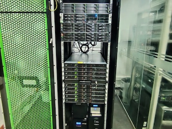Rack de servidores con múltiples unidades de almacenamiento y procesamiento, cableado y un panel lateral verde perforado en una sala técnica