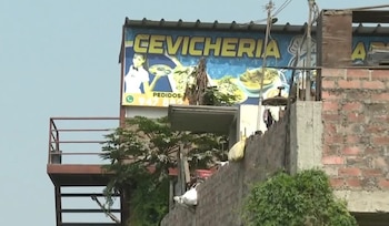 Un cartel publicitario de una cebichería sobre una edificación de ladrillo con una escalera metálica exterior y vegetación