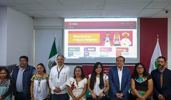 Diez personas, incluyendo a hombres y mujeres, posan de pie frente a una pantalla que muestra la sección de CONDUSEF de "Materiales en lenguas indígenas" y banderas mexicanas