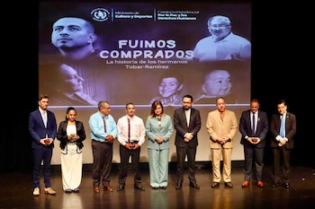 Nueve personas en un escenario frente a una pantalla con texto 'Fuimos Comprados', logotipo de Guatemala, y retratos de adultos y niños. Algunos sostienen cajas