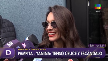 Mujer con gafas de sol, pelo castaño y labios rojos sonríe. Varios micrófonos. Banner inferior con texto 'Pampita - Yanina: tenso cruce y escándalo'. Logotipo de canal