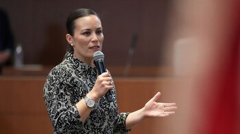 Gina Ortiz Jones, vestida con una camisa blanca y negra, habla en un micrófono, con su mano izquierda levantada en un gesto