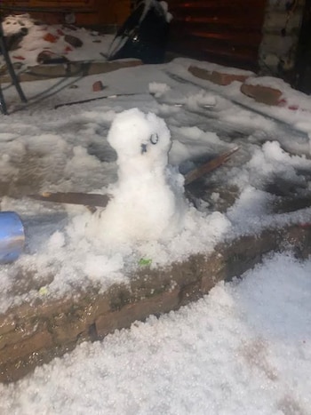 Una pequeña figura de nieve y granizo con alas de madera sobre una superficie de ladrillo rodeada de hielo acumulado