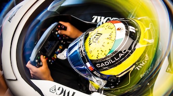 Vista superior de un piloto con casco amarillo que sostiene el volante con botones en el interior de un automóvil de carreras.