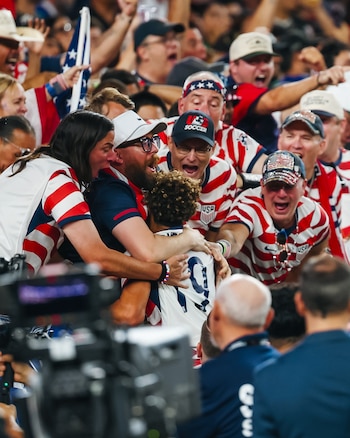 Un futbolista con el dorsal nueve abraza a aficionados con ropa con la bandera de Estados Unidos en la grada