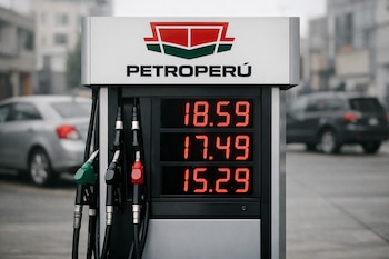 Primer plano de un surtidor de gasolina Petroperú con precios digitales elevados en pantalla. Al fondo, autos estacionados en una calle urbana con edificios desenfocados.
