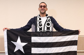 Un hombre con gafas de sol y bufanda sostiene con ambas manos una bandera de franjas negras y blancas con una estrella