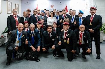 Un grupo de personas, mayormente hombres, posa para una foto. La mujer está en el centro. Visten traje, corbata, medallas, insignias y boinas