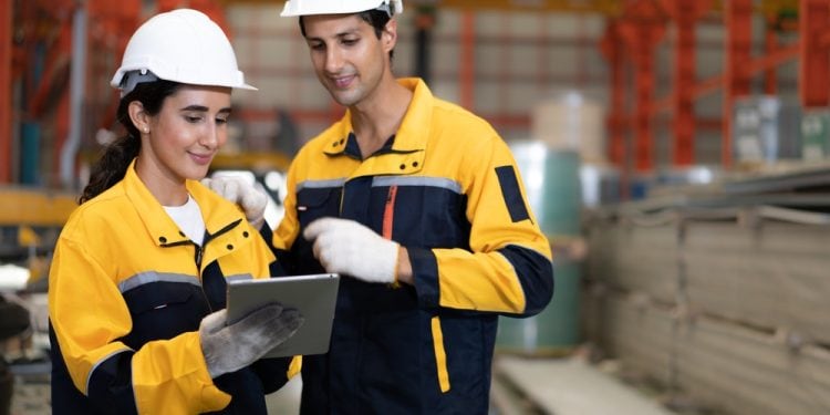 Dos empleados de la empresa Bartlett Cocke con cascos de protección y uniformes de seguridad examinan un proyecto en una tableta electrónica dentro de una nave industrial. (Banco Centroaméricano de Integración Económica)