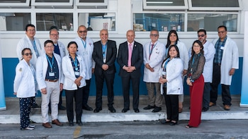 Un grupo de doce profesionales, la mayoría vistiendo batas blancas de laboratorio, posan de pie al aire libre frente a un edificio con ventanas