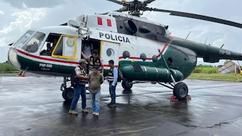 Agentes de la Policía Nacional del Perú custodian a un detenido frente a un helicóptero policial en una pista mojada