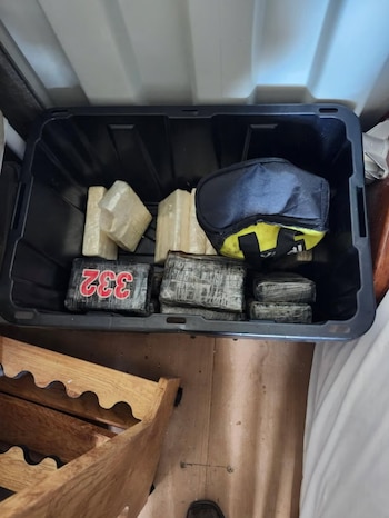 Una caja de plástico negro contiene varios paquetes rectangulares envueltos en cinta adhesiva y un bolso de color negro con amarillo