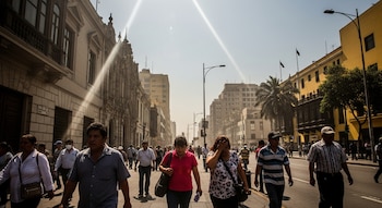 Vista de una calle concurrida en Lima bajo un sol intenso, donde peatones caminan por la acera y la calle. Rayos de sol penetran desde el cielo claro.
