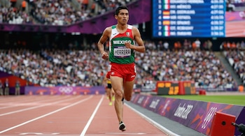 Eduardo Herrera, fondista mexicano, corre en una pista de atletismo con uniforme verde, blanco y rojo; público en gradas al fondo.