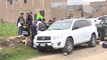 Vehículo SUV blanco en un camino de tierra, con varios efectivos policiales y otras personas alrededor; se observan construcciones al fondo y vegetación a un lado