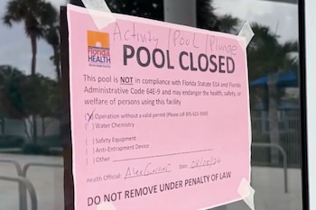 Cartel rosa pegado en una puerta de vidrio de piscina. El cartel dice "PISCINA CERRADA" y menciona "Operación sin permiso válido", con logo de Florida Health