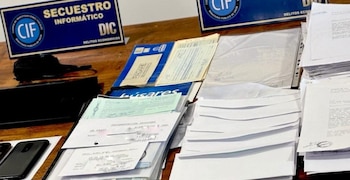 Pilas de billetes de 20.000 pesos, 100 dólares y euros, una laptop, smartphones, pasaporte, documentos y carteles de 'SECUESTRO DINERO' sobre una mesa de madera