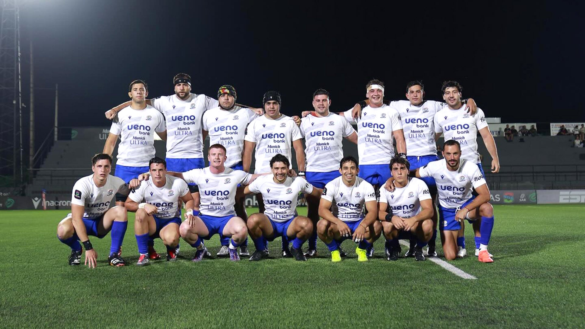 El equipo de rugby Yacaré XV posa en grupo sobre el campo de juego de noche, luciendo sus uniformes blancos y azules, listo para el partido (@yacarexv)