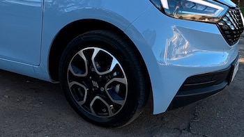Rueda delantera con llanta de aleación y parte frontal de un automóvil de color azul claro estacionado sobre tierra