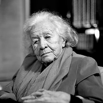 Retrato en blanco y negro de una mujer mayor con cabello blanco y rizado, mirando al frente. Viste un chal oscuro y sus manos están entrelazadas