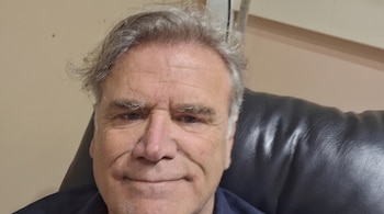 Primer plano del rostro de un hombre con cabello canoso y camisa oscura reclinado en un sillón de cuero.