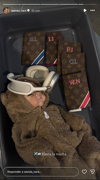 Un bebé con traje de oso marrón y auriculares blancos en la cabeza, junto a cinco pasaportes marrones de Louis Vuitton con iniciales en una bandeja gris