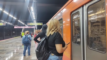 Vista de la plataforma de la estación Universidad del Metro con un tren naranja parado. Varias personas esperan junto al andén bajo luces LED modernas
