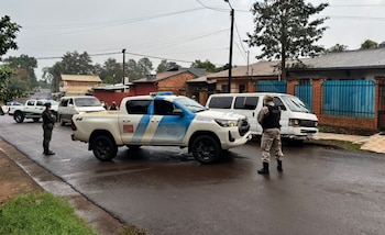 Vista de una calle mojada con dos camionetas policiales, una blanca Toyota Tacoma y una verde, junto a una furgoneta blanca dañada. Dos agentes uniformados están de pie