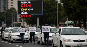Caravana de taxis blancos en una calle. Personas sostienen carteles "NO AL SUBSIDIO". Un cartel electrónico muestra precios de combustible: Regular, Súper, Diésel.