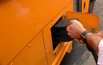 Manos de una persona que insertan un conector de carga negro en el compartimento lateral de un autobús escolar amarillo