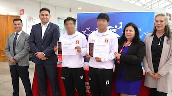 Seis personas posan. Dos jóvenes en chándal blanco sostienen certificados. Dos hombres con traje y dos mujeres acompañan. Al fondo, un banner del IPD
