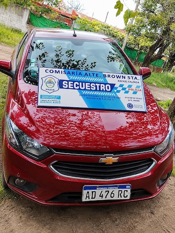 Automóvil rojo de marca Chevrolet con una placa policial de secuestro colocada sobre el capó y matrícula delantera argentina