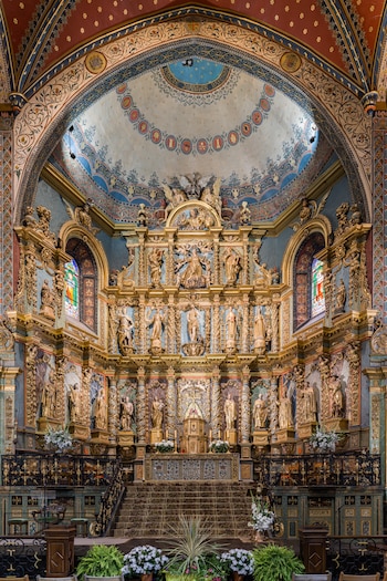 Un retablo de varios metros de altura separado en tres pisos que alberga diferentes figuras cristianas. La decoración es rica y opulenta.
