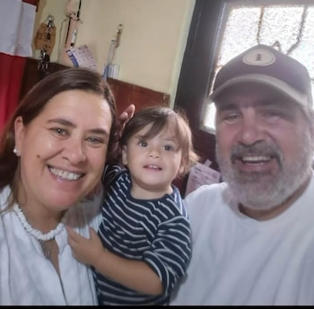 Selfie de una mujer sonriente, un niño pequeño en brazos y un hombre sonriente con gorra a la derecha. Todos miran a la cámara