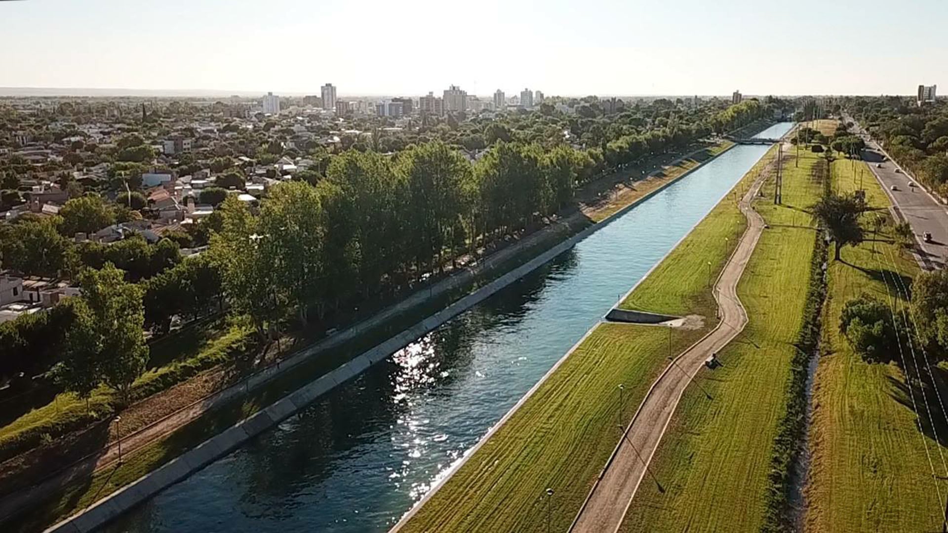 Una vista aérea del canal principal de riego fluyendo a través de General Roca, con áreas verdes, caminos peatonales y el perfil urbano de la ciudad al fondo (Facebook)